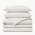 Stacked White Stripe cotton sateen bedding set on a warm off-white background